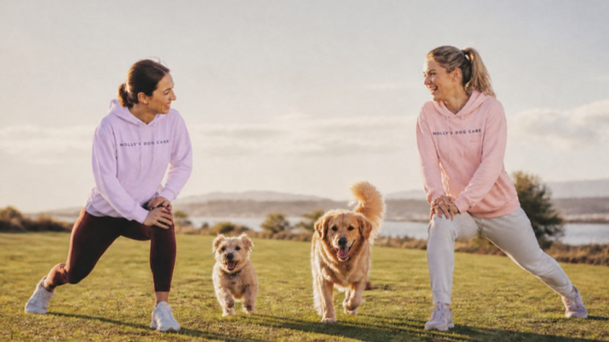 Two women in Molly's crop hoodies stretching in the park with their dogs