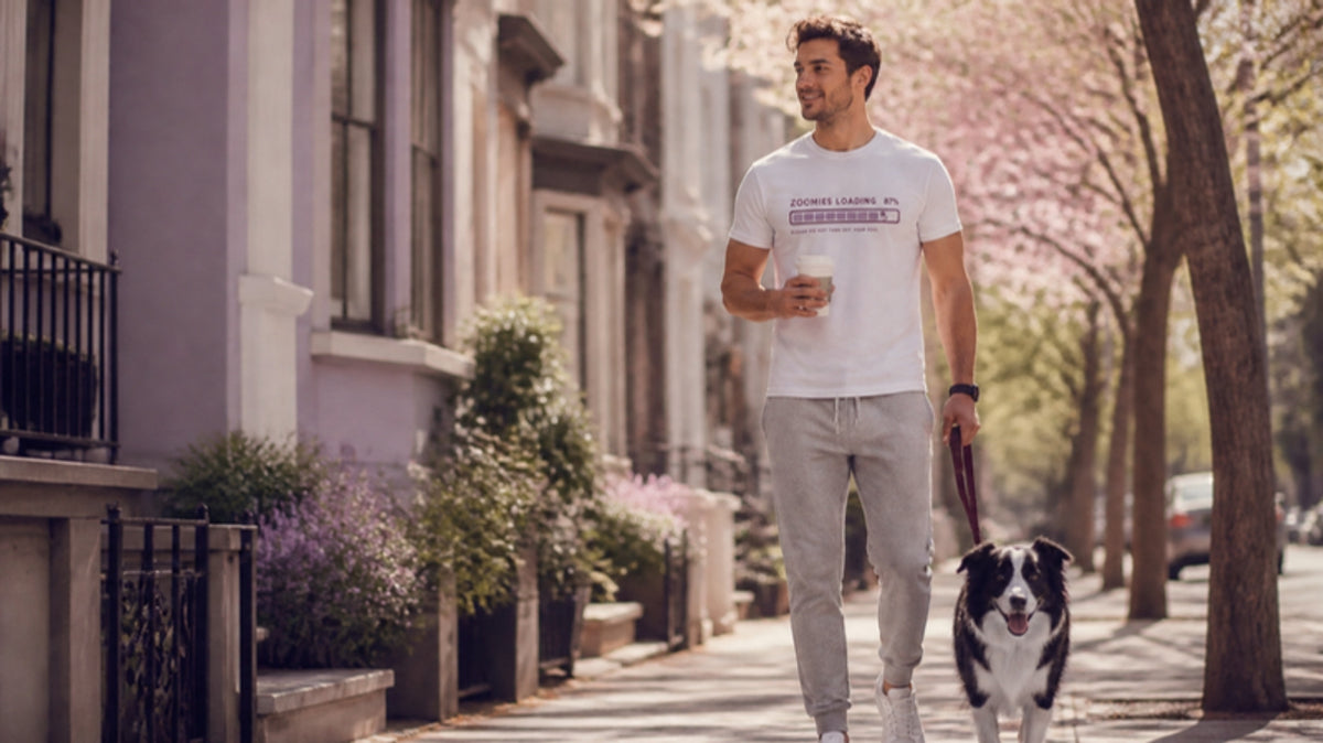 Man in the Zoomies Loading tee walking his border collie with a coffee